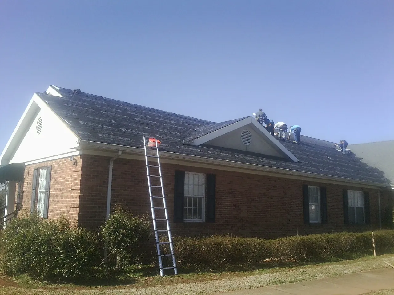 Crew tearing shingles off a brick ranch roof with a ladder set — Metal Roof Repair work by our crew in Portsmouth